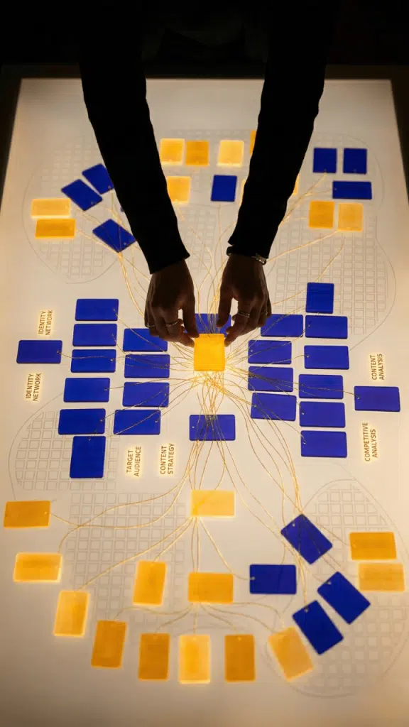 Stratégie de contenu GEO : mains organisant un réseau de cartes thématiques interconnectées sur une table lumineuse pour structurer la visibilité dans les moteurs génératifs